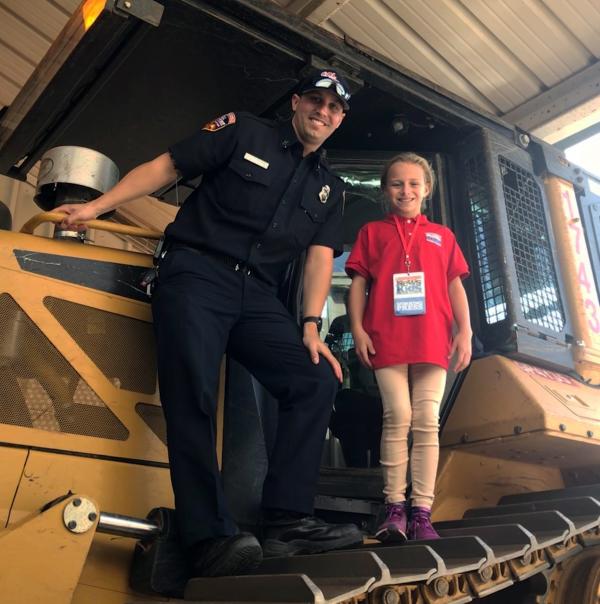 Ella and Captain Scott Kenney stand on a bulldozer that Cal Fire uses to fight wildfires.