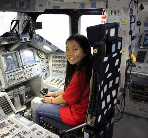 Bridget sits inside the cockpit of a space shuttle mockup.