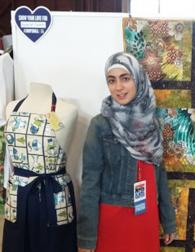 I am standing next to a handmade quilt and apron. I am standing next to a handmade quilt and apron.